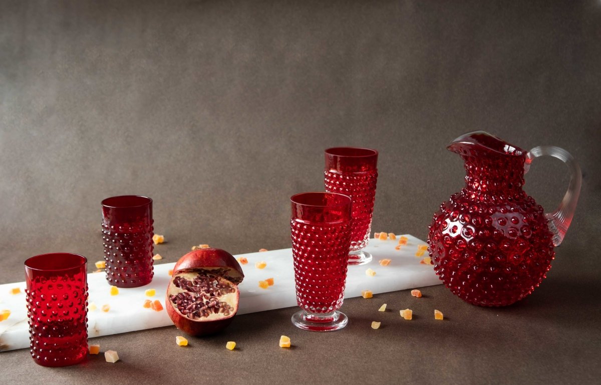 Underlay Garnet Hobnail Tumblers surrounded by products from the Hobnail collection and fruit on a black background