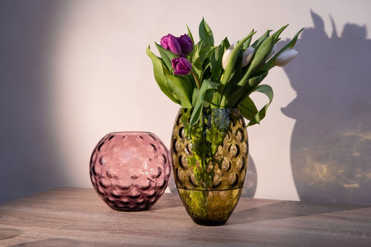Violet Kugel Vase next to on a wooden table with white and purple flowers, as well as a white background and flower shadows