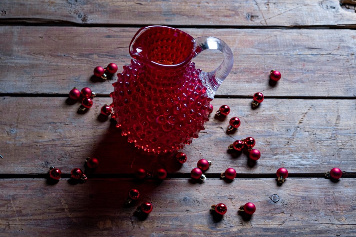 Underlay Garnet Hobnail Jug on a wooden table surrounded by small red Christmas baubles