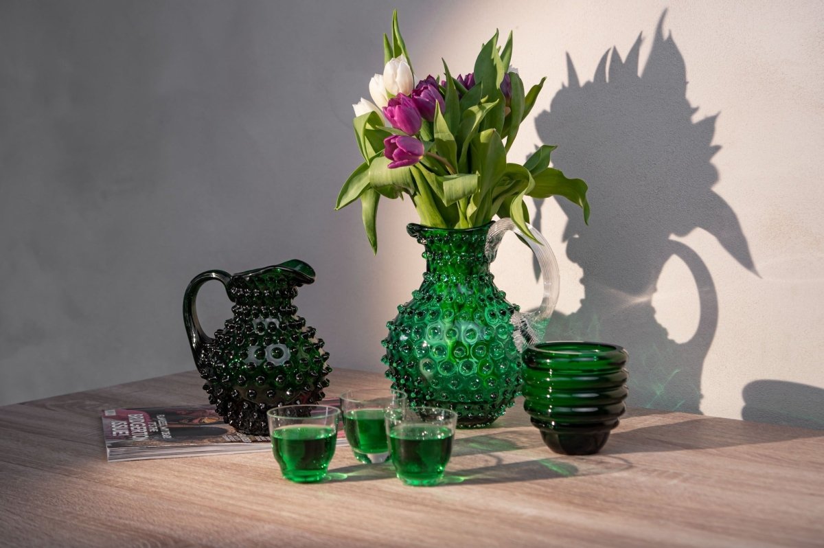 Underlay Dark Green Hobnail Jug on a wooden table with flowers and a white wall with shadows