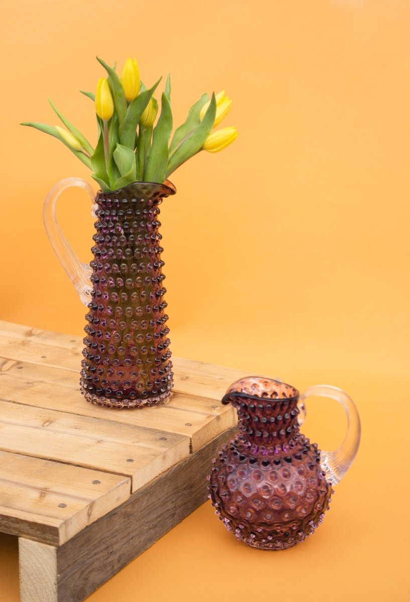 Underlay Violet Hobnail Jug Small on a wooden pallet with yellow flowers and an orange background
