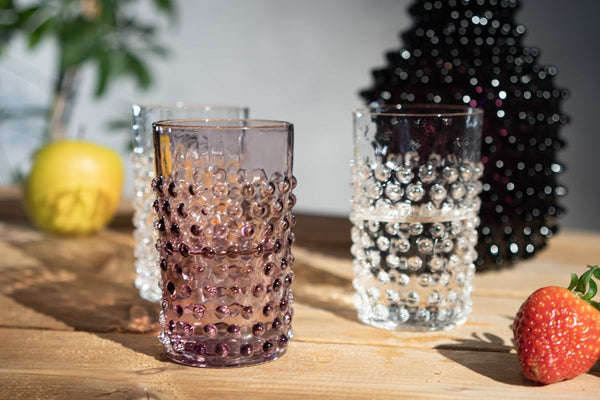 Underlay Violet Hobnail Tumblers on a wooden table surrounded by objects from the Hobnail collection and fruit.