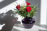Violet Marika Vase Large on a white piece of furniture with a bouquet of red and white flowers, with shadows and a white background