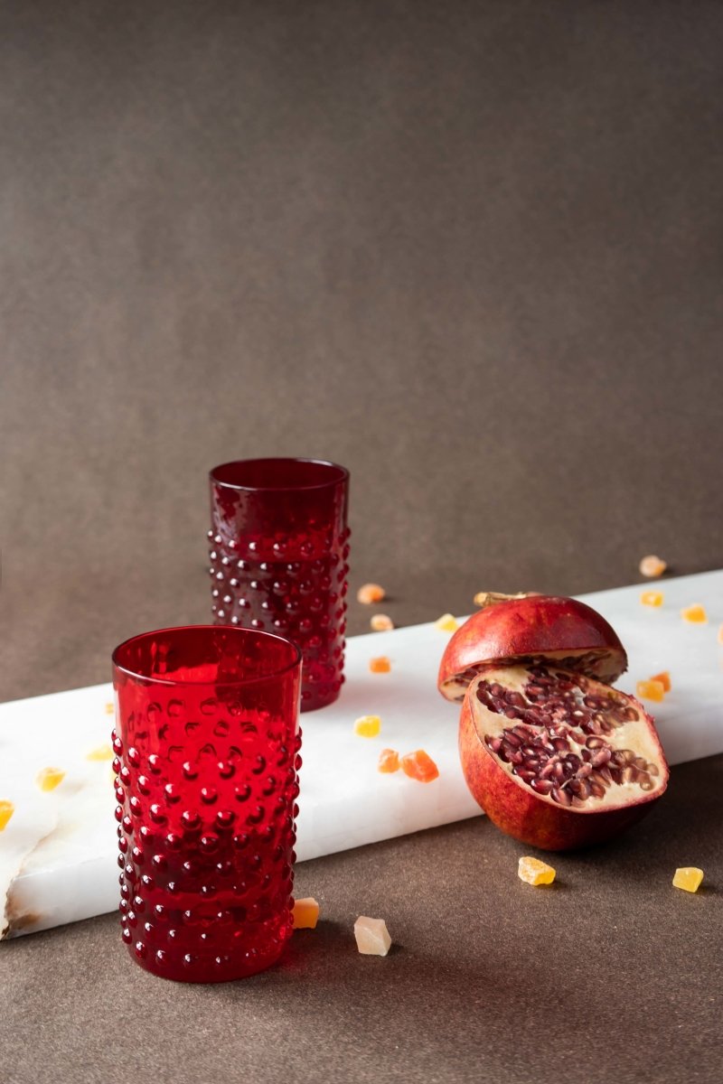 Underlay Garnet Hobnail Tumblers surrounded by products from the Hobnail collection and fruit on a black background 